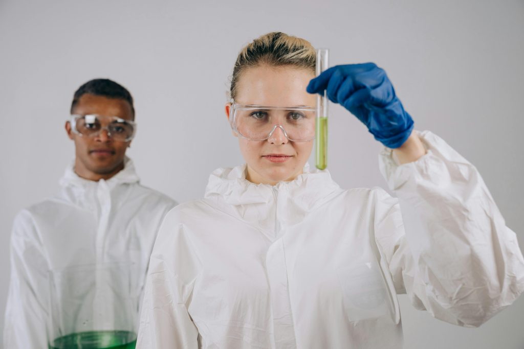 Two scientists in lab coats and protective gear conducting a chemical experiment with a test tube.